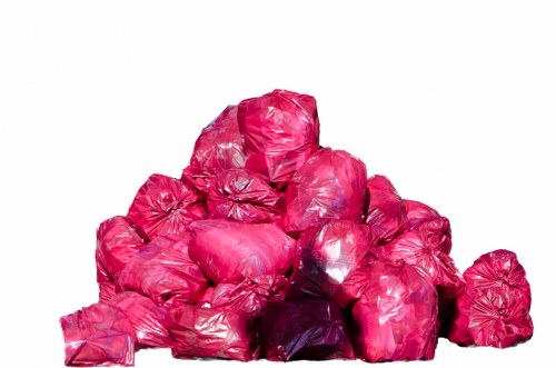 A large pile of pink plastic rubbish bags, tightly knotted at the top, stacked on a white background. The bags appear to be filled with garden or household waste, with some bags showing slight creases and folds in the plastic material. The pile is arranged in a somewhat pyramid shape, with smaller bags supporting larger ones at the base. The lighting is even, highlighting the shiny, reflective surface of the plastic bags. This image is typical of waste collection or clearance activities, possibly related to garden clearance services in Hillingdon, as offered by Garden Clearance Hillingdon, a company specializing in rubbish removal. The scene is clean and straightforward, emphasizing the volume of waste that may be handled during rubbish or garden clearance projects within the local area, including Hillingdon or nearby UB postcode districts.